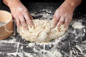 baker kneads white wheat flour dough on a black wooden table