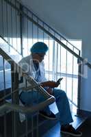Male surgeon using mobile phone while sitting on stairs at hospital