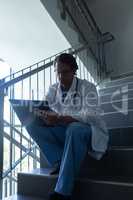 Male surgeon writing on clipboard while sitting on stairs at hospital