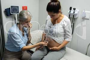 Female doctor examining pregnant womans belly with stethoscope in examination room