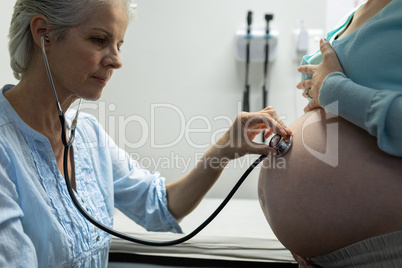 Doctor examining pregnant woman belly with stethoscope