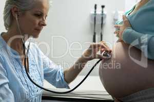 Doctor examining pregnant woman belly with stethoscope