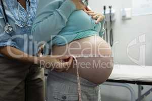 Female doctor measuring pregnant woman belly in examination room