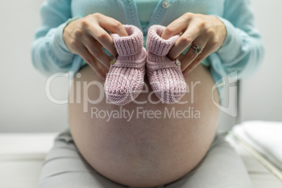 Pregnant woman holding baby shoes in hospital