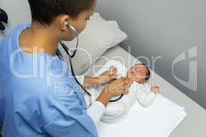 Female doctor examining baby with stethoscope in medical examination room