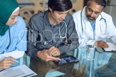 Medical team discussing x-ray report over digital tablet at table in hospital