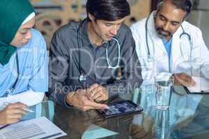 Medical team discussing x-ray report over digital tablet at table in hospital