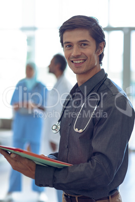 Male doctor holding medical file and looking at camera in hospital