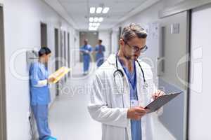 Male doctor writing on clipboard in corridor at hospital