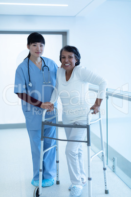 Female doctor helping female patient to walk with walker in the corridor