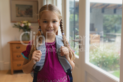 Cute girl with school bag looking at camera in a comfortable home