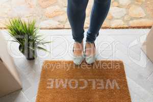 Woman standing near welcome mat in front of door at home