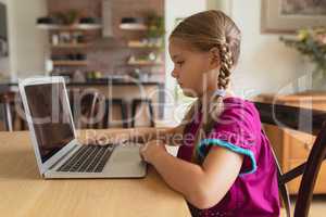 Cute girl using laptop on dining table in a comfortable home