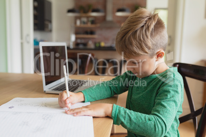 Cute boy doing homework at dining table in a comfortable home