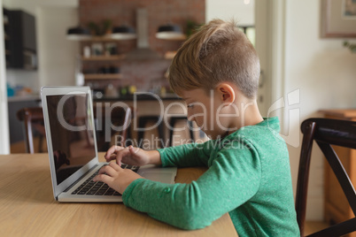 Cute boy using laptop at dining table in a comfortable home