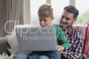 Father and son using laptop on sofa in a comfortable home