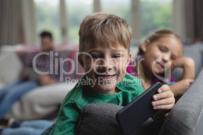 Cute boy with mobile phone looking at camera on sofa in a comfortable home