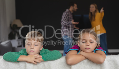 Sad kids leaning on sofa while parents arguing in background