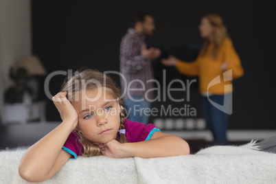 Sad girl leaning on sofa while parents arguing in background