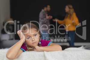 Sad girl leaning on sofa while parents arguing in background