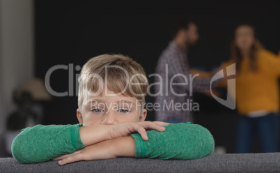 Sad boy leaning on sofa while parents arguing in background