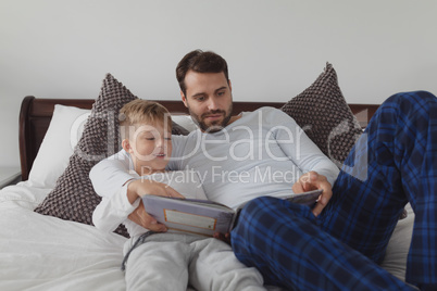 Father and son reading a story book while lying on bed in bedroom