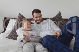 Father and son reading a story book while lying on bed in bedroom
