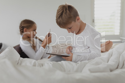 Siblings using digital tablet on bed in bedroom at comfortable home