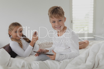 Siblings using digital tablet on bed in bedroom