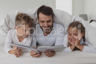 Father and children reading a book under blanket