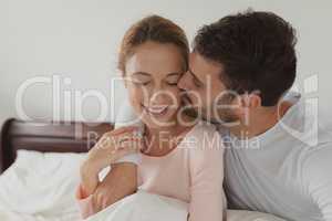 Man kissing woman on bed in bedroom