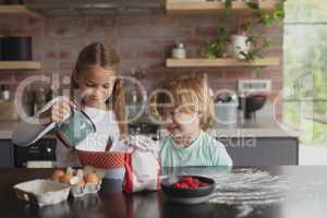Siblings preparing cookie on worktop in kitchen