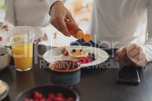 Man pouring honey on pancake at dining table