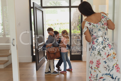 Father embracing his children as he enters the house while mother looking them