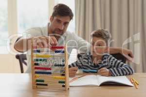 Father teaching his son mathematics with abacus in a comfortable home