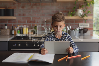 Boy using digital tablet at table in kitchen at home Boy using digital tablet at table in kitchen at home