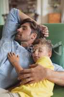 Father and son sleeping together on a sofa in living room