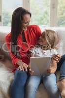 Mother and daughter using digital tablet in living room