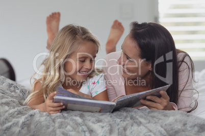 Mother and daughter reading a story book in bedroom