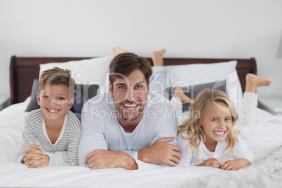 Father and children lying together on bed in bedroom at home