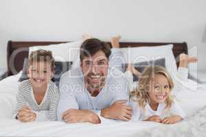 Father and children lying together on bed in bedroom at home