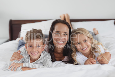 Mother and children lying together on bed in bedroom at home