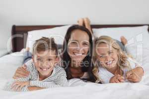 Mother and children lying together on bed in bedroom at home