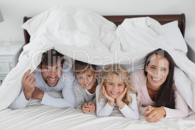 Family lying together under blanket in bedroom at home