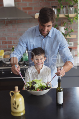 Father and son preparing vegetable salad in kitchen