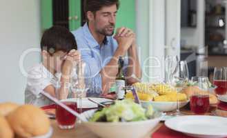 Father and son praying before having lunch at dining table