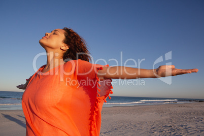 Beautiful woman with arms stretched out standing on beach in the sunshine