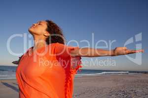 Beautiful woman with arms stretched out standing on beach in the sunshine
