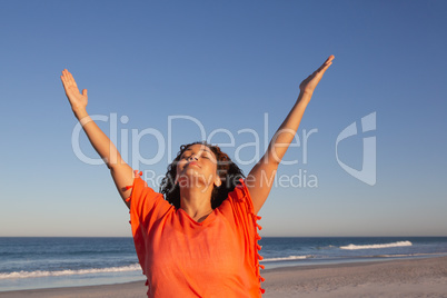 Beautiful woman with arms up standing on beach in the sunshine