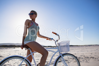 Woman in sunglasses sitting on bicycle at beach in the sunshine